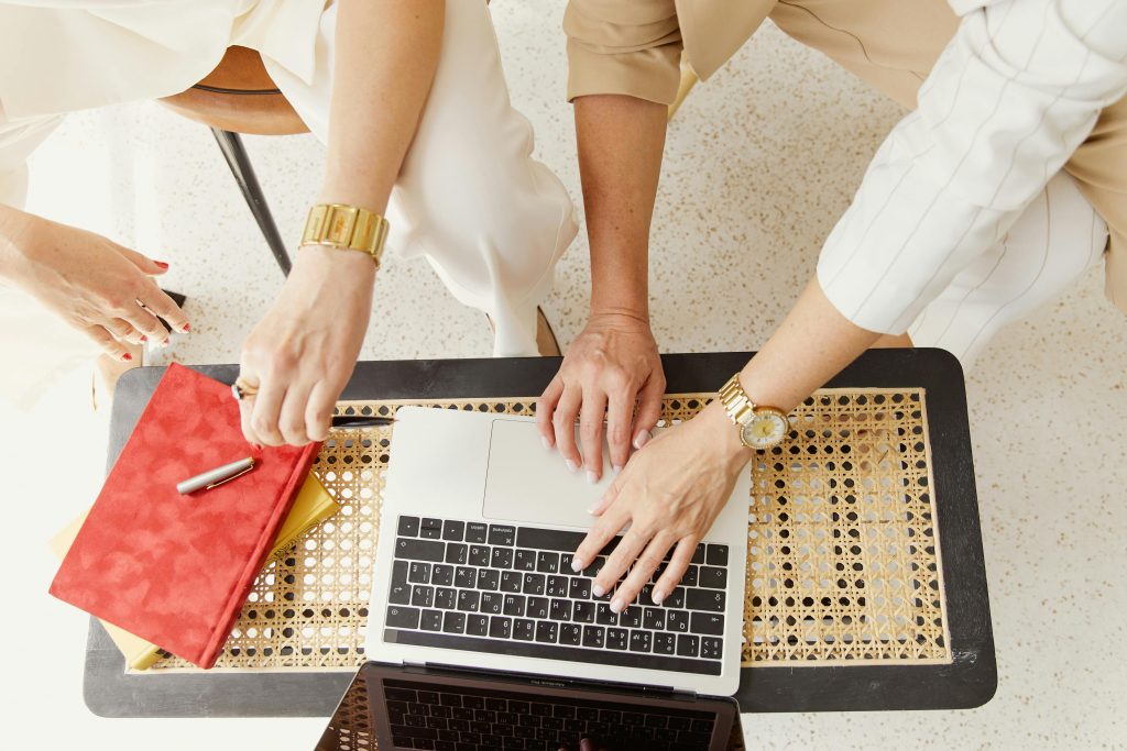Hands of business professionals on a laptop and notebook, collaborating in a bright workspace.